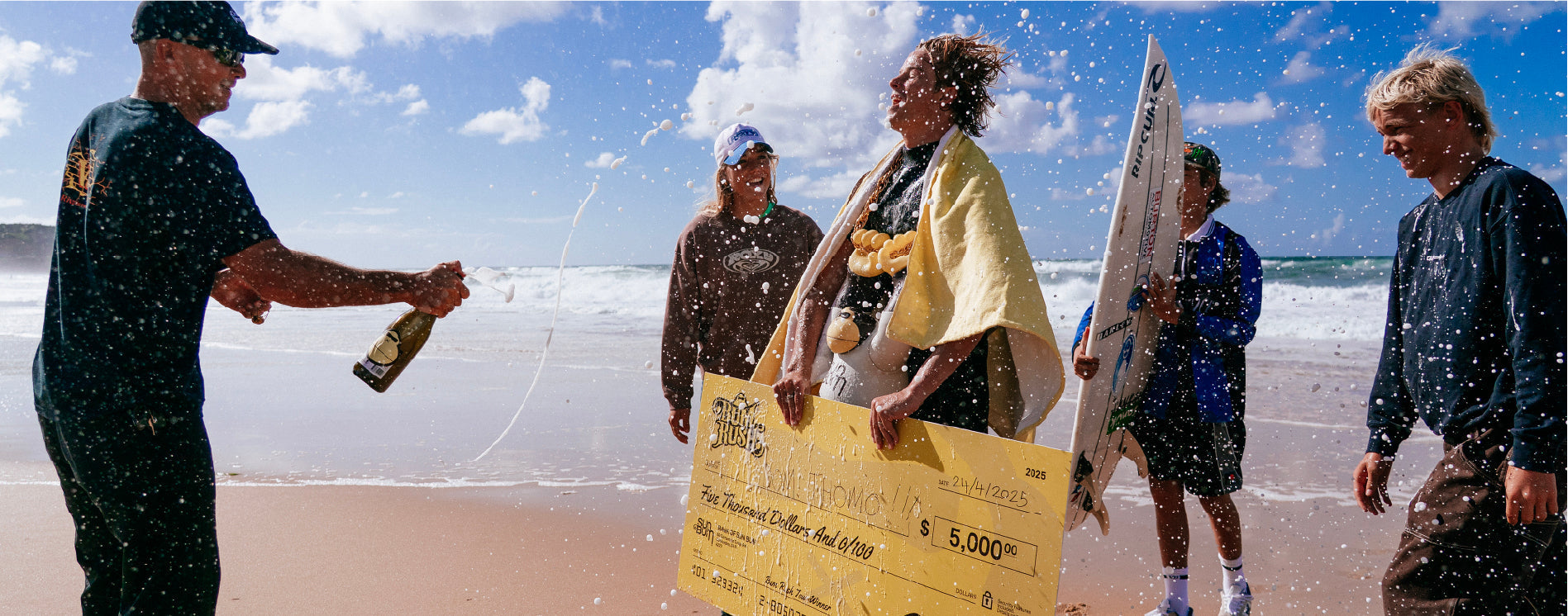 Person holding a large check on a beach with others in the background