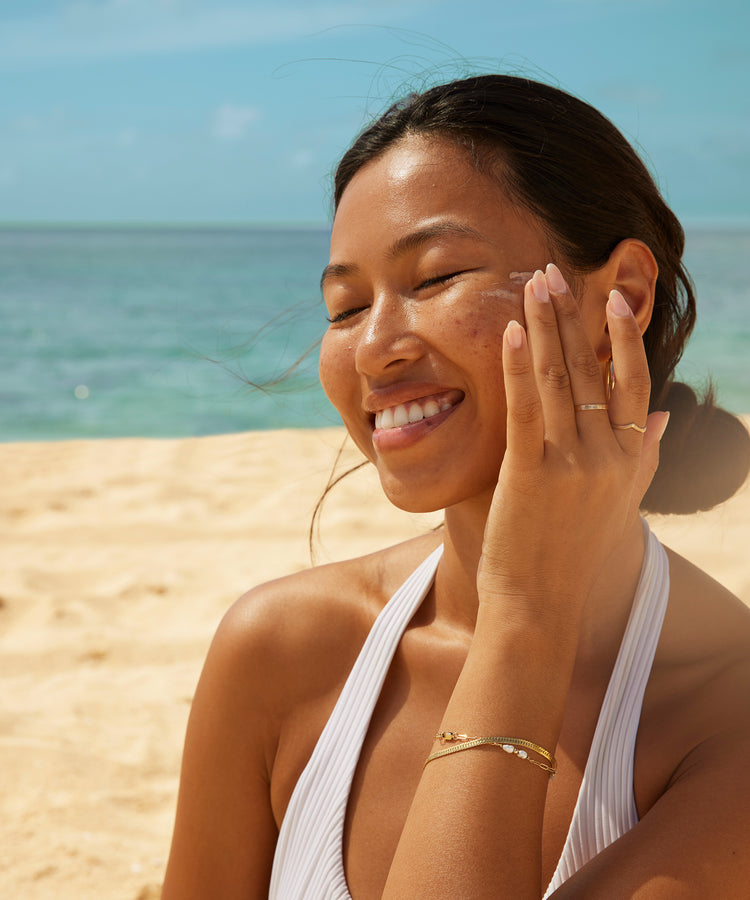 Woman applying sunscreen on a beach with ocean view