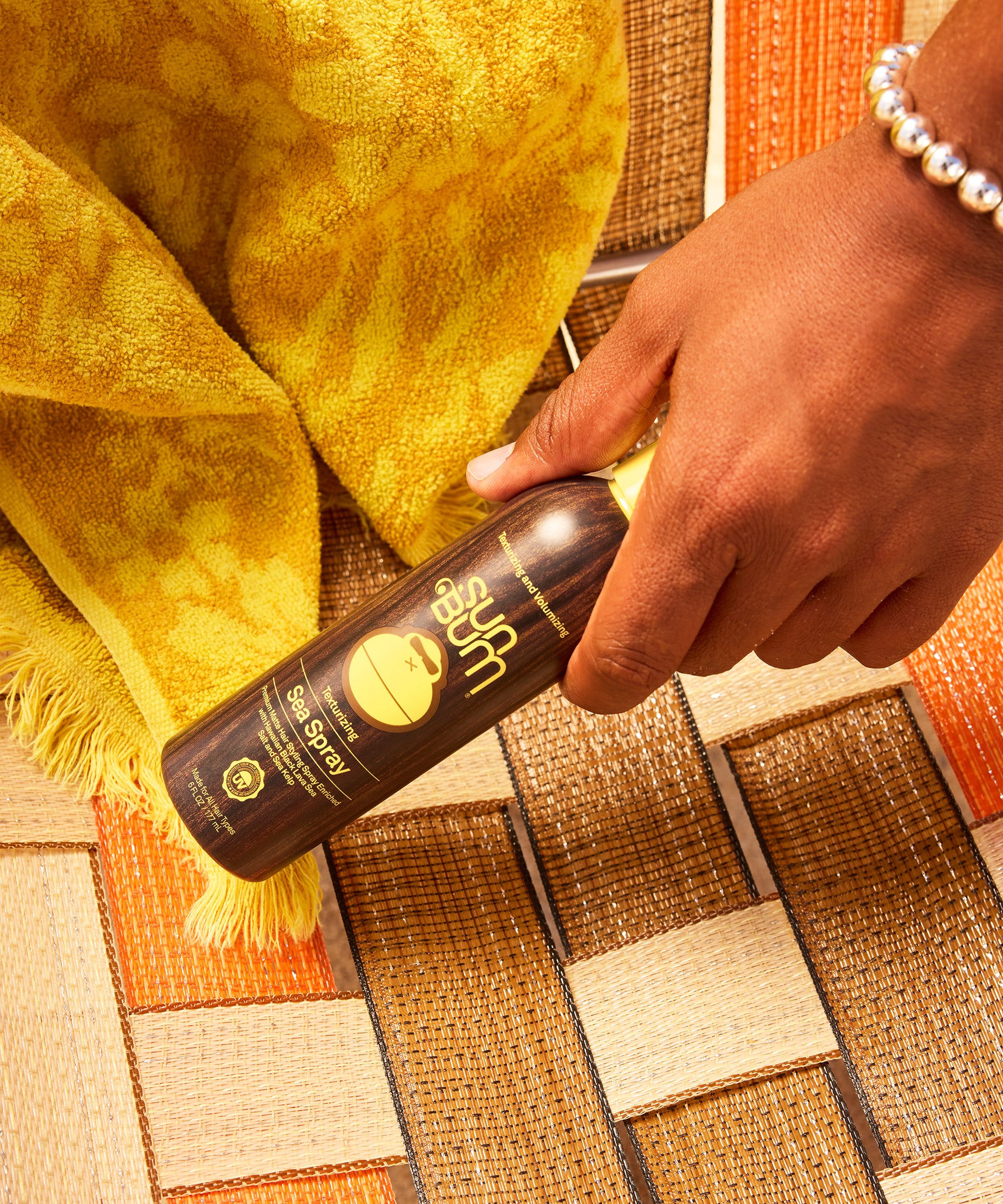 Hand holding a bottle of Suu Sun spray on a textured surface with a yellow towel.