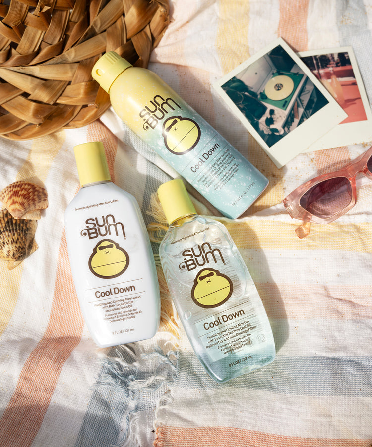Sun Bum Cool Down products on a beach setting with sunglasses and seashells.