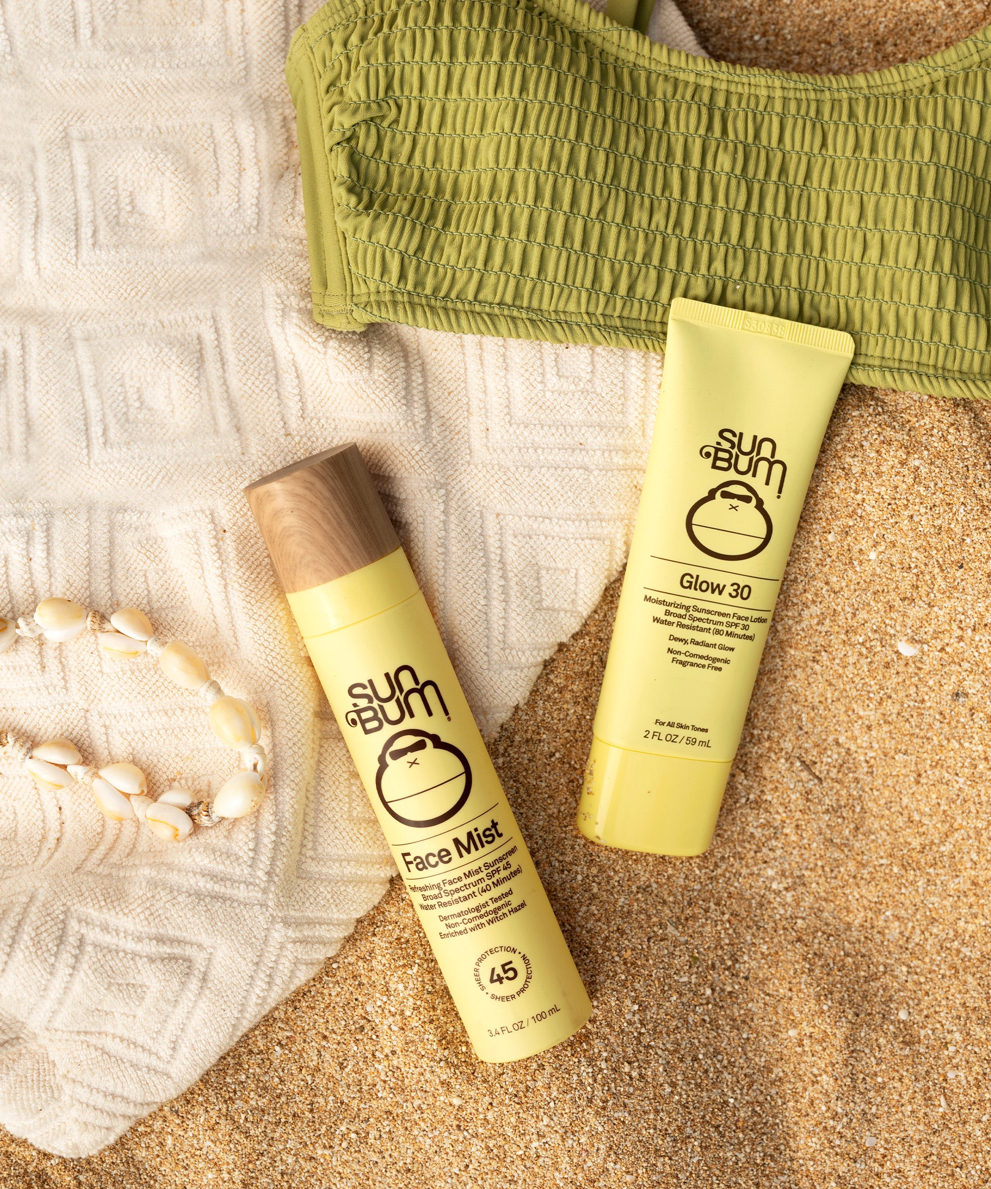 Sun Bum Face Mist and Glow 30 sunscreen on sand with green top.