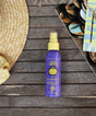 Sun Bum Tone Enhancer spray bottle on a wooden surface with a hat and sunglasses in the background.