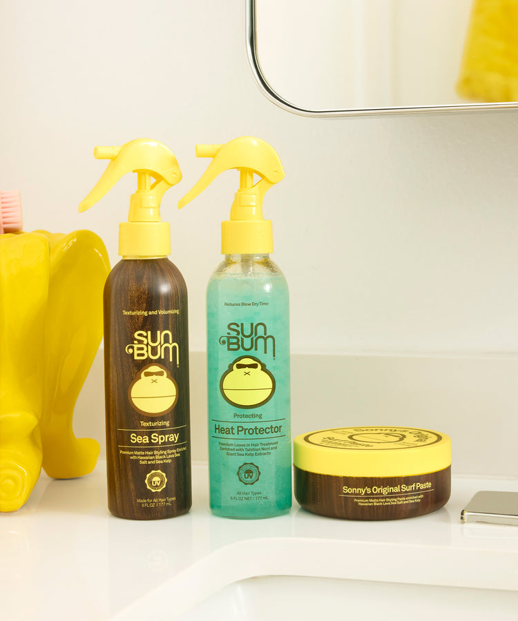Sun Bum skincare products including sea spray, heat protector, and surf balm on a bathroom counter.