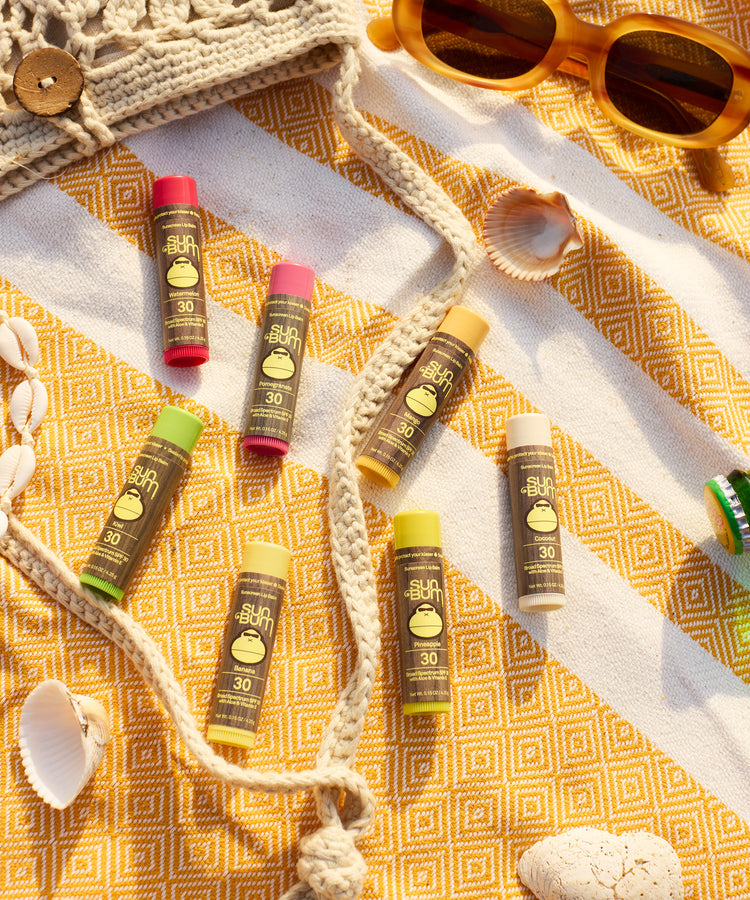 Sunscreen bottles with SPF 30 on a yellow patterned towel with sunglasses and shell decorations.
