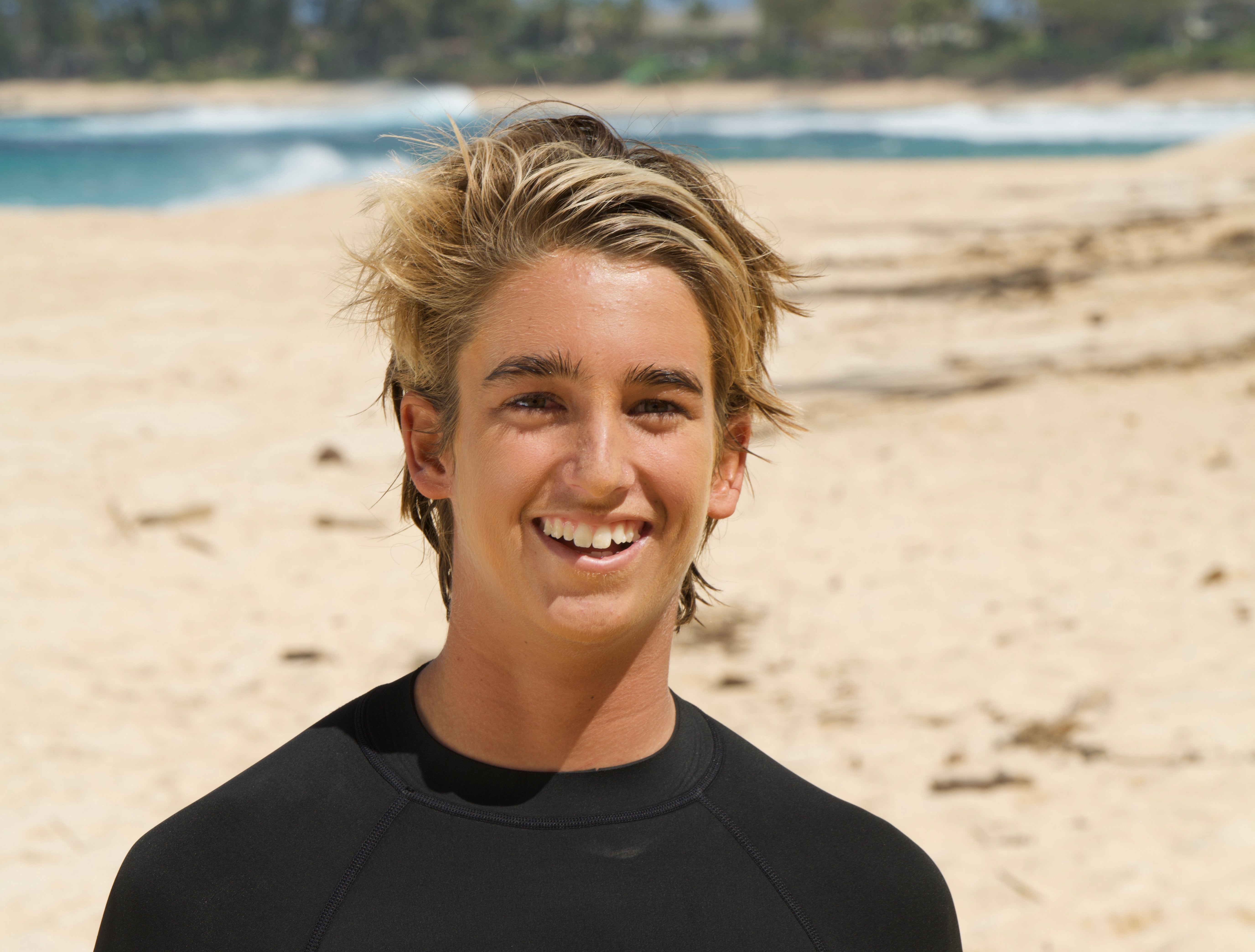 Person wearing a black wetsuit on a beach with ocean in the background