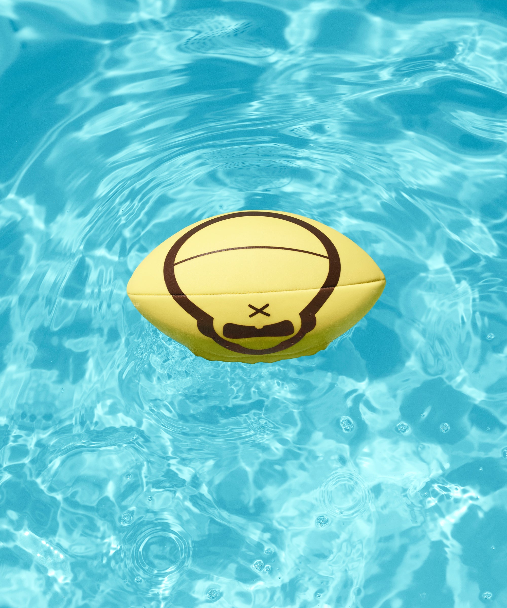 Yellow Sonny football floats in a clear blue pool, perfect for sunny day fun - Sonny Gear Collection - Sun Bum