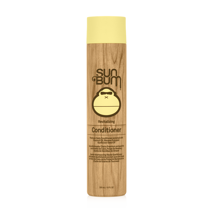 A bottle of Sun Bum Revitalizing Conditioner with a beige label featuring the brand's logo and the text 'NEW DELICAMUM'. The bottle is tall and slender with a wooden appearance.